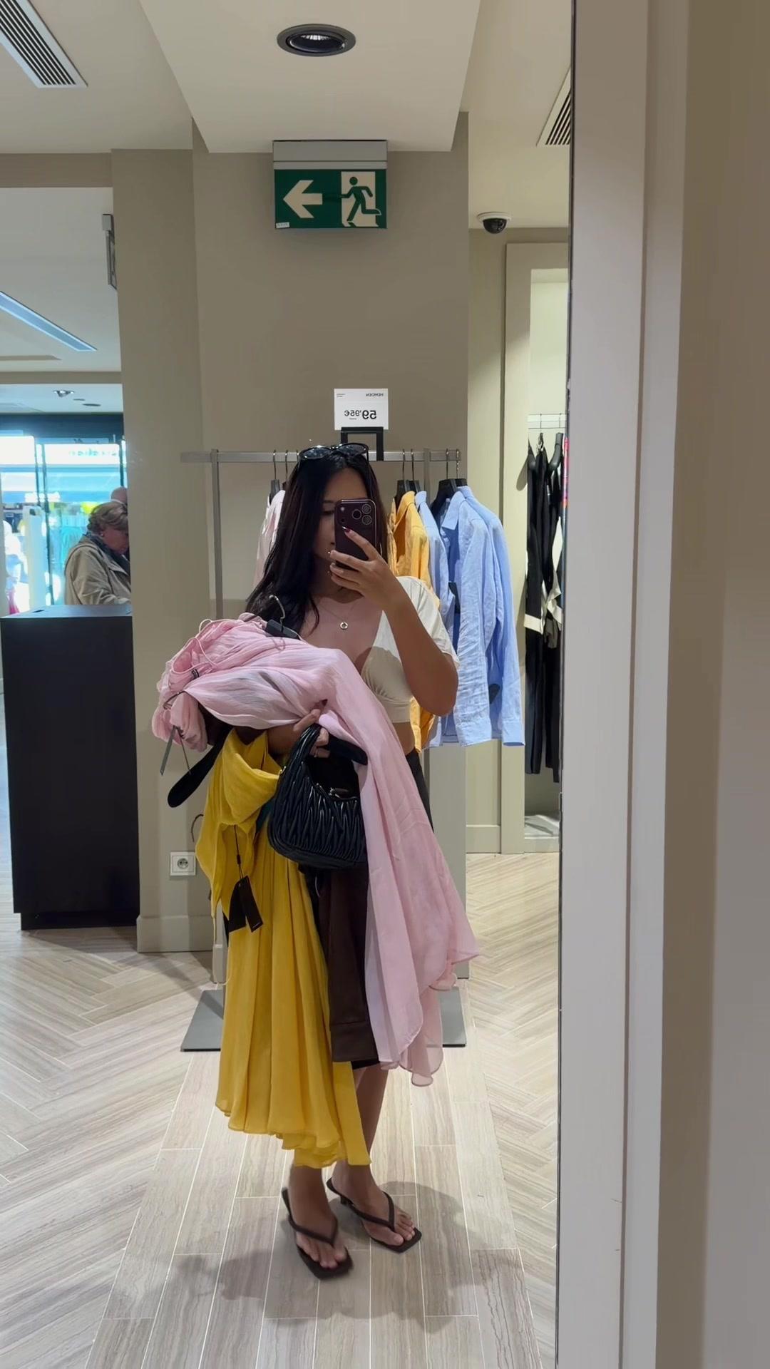 Woman Holding Clothes in Clothing Store Mirror